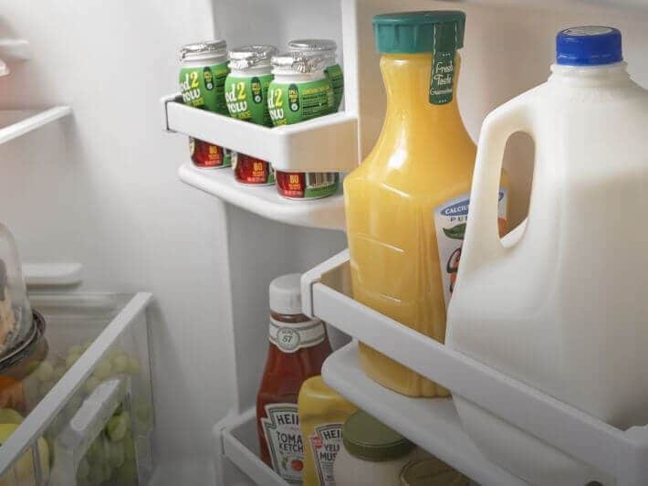 A door storage bin filled with a milk carton, orange juice and other condiments. A door storage bin filled with a milk carton, orange juice and other condiments.