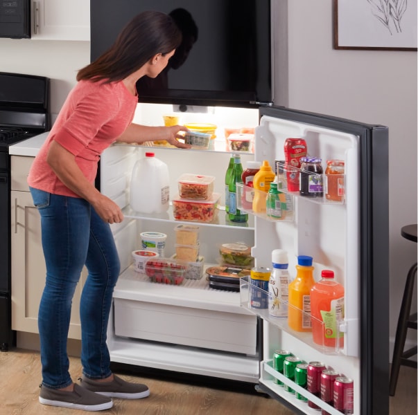 A person pulling an item out of an Amana® refrigerator.