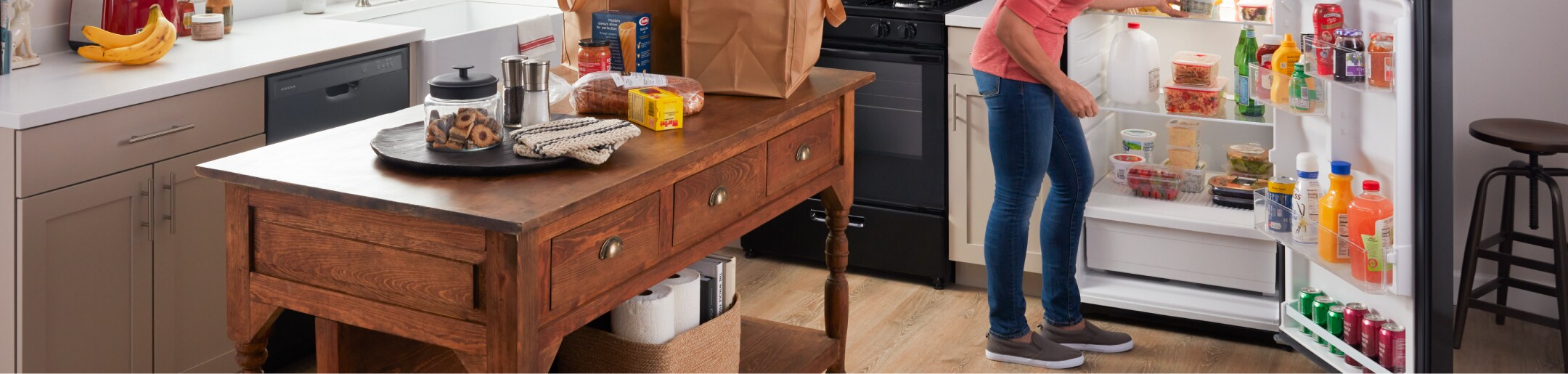 A person putting groceries into an Amana® refrigerator.