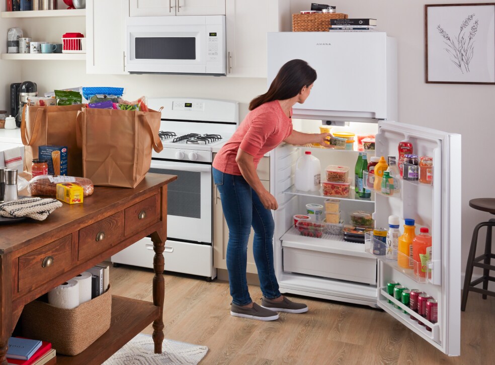 A person putting groceries into an Amana® refrigerator.