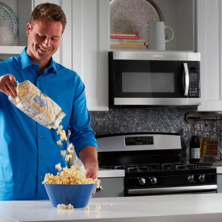 Person pouring popcorn into bowl in kitchen with Amana® range and microwave