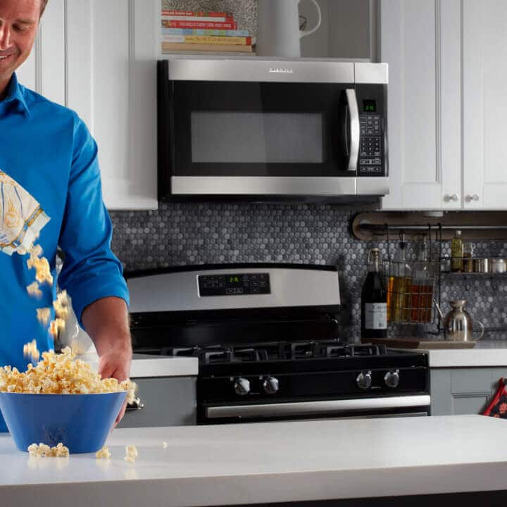 Person pouring popcorn into bowl in kitchen with Amana® range and microwave
