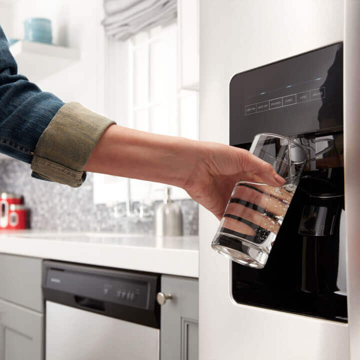 Person filling a glass from a refrigerator water dispenser