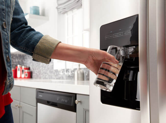 Person filling a glass from a refrigerator water dispenser
